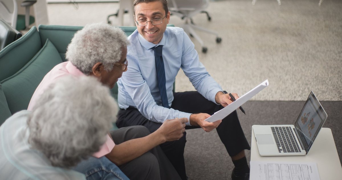 Conseiller présentant un plan à deux clients avec documents et ordinateur portable
