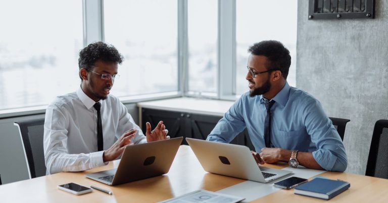 Deux professionnels échangent autour d'une table de réunion, ordinateurs portables ouverts