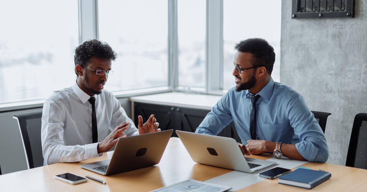 Deux professionnels échangent autour d'une table de réunion, ordinateurs portables ouverts