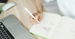 Main qui note un plan d'articles dans un carnet à côté d'un ordinateur portable