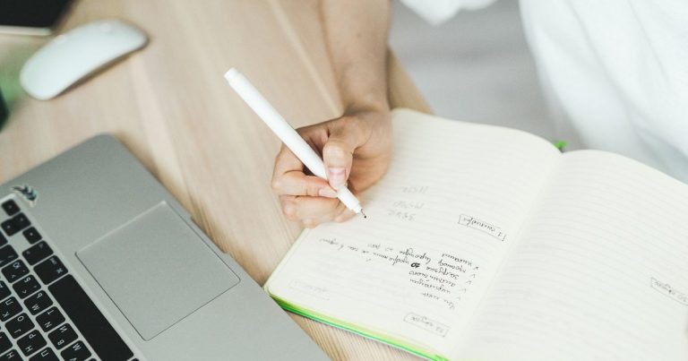 Main qui note un plan d'articles dans un carnet à côté d'un ordinateur portable