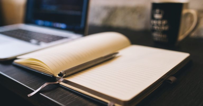 Carnet ouvert et stylo sur un bureau en bois à côté d'un ordinateur portable
