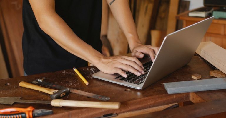 Artisan consultant internet sur un ordinateur portable parmi ses outils de menuiserie