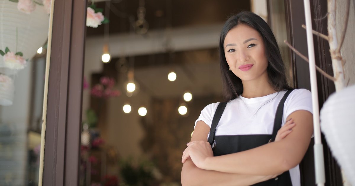 Jeune commerçante souriante, bras croisés, à l'entrée de sa boutique