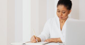 Femme écrivant des notes à un bureau à côté d'un ordinateur portable
