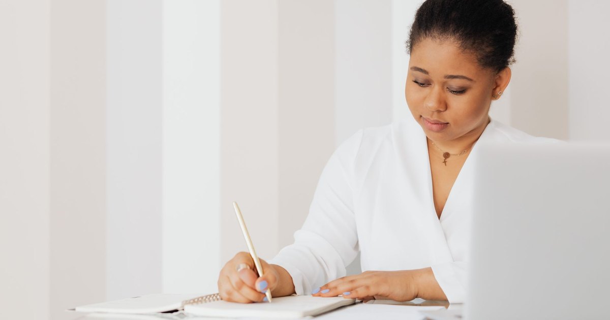 Femme écrivant des notes à un bureau à côté d'un ordinateur portable
