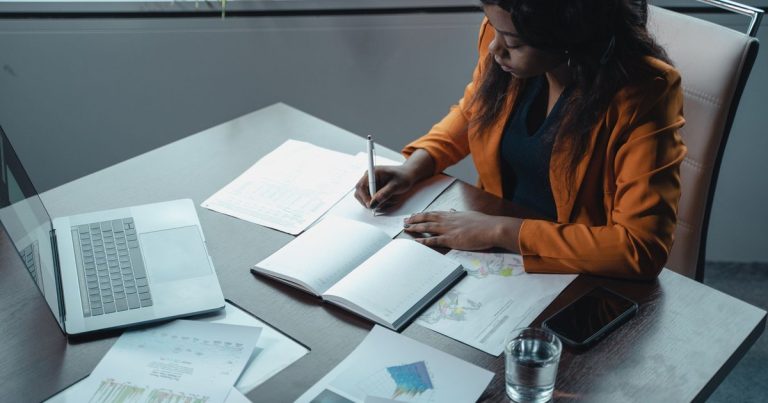 Femme prenant des notes à son bureau avec documents et ordinateur portable