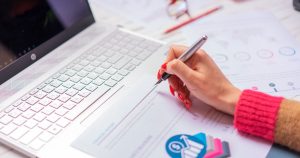 Main avec un stylo analysant des graphiques à côté d’un ordinateur portable