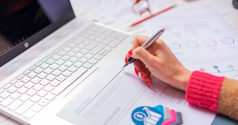 Main avec un stylo analysant des graphiques à côté d’un ordinateur portable