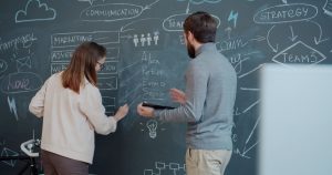 Deux collègues réfléchissant à une stratégie devant un tableau noir couvert de schémas