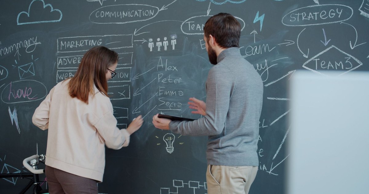 Deux collègues réfléchissant à une stratégie devant un tableau noir couvert de schémas